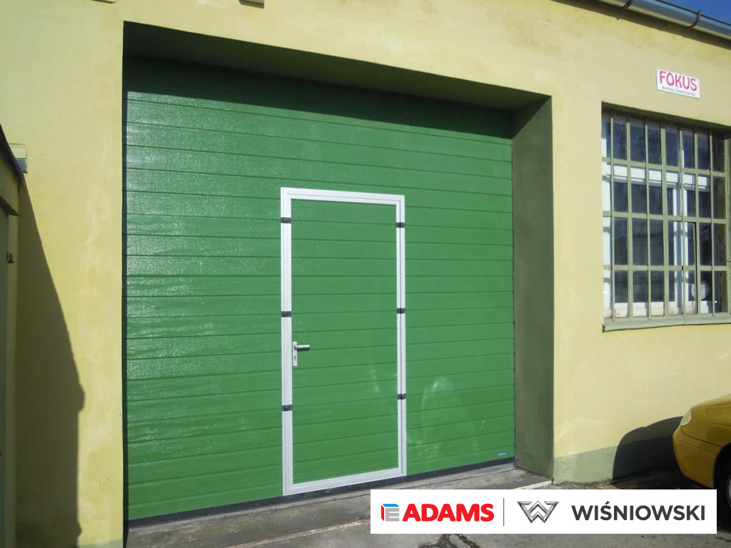 Brama przemysłowa segmentowa Wiśniowski Makropro z drzwiami przejściowymi, struktura panela: woodgrain, kolor: RAL:6005