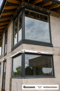 Nasze realizacje – Wiśniowski – Brama segmentowa UniTherm, okna PVC PRIMO 82, rolety zewnętrzne  Szukasz stolarki dla swojego domu, który ma być zarówno estetyczny, jak i energooszczędny? Zobacz naszą realizację, gdzie zastosowaliśmy kompleksowe rozwiązania Wiśniowski, gwarantujące funkcjonalność i niezawodność.  Lokalizacja realizacji: Drozdów  Okna PVC PRIMO 82 W tym projekcie postawiliśmy na okna PVC PRIMO 82, które wyróżniają się  świetnymi właściwościami izolacyjnymi. Na zewnątrz są w nowoczesnym kolorze - ciemnoszary jedwab, który idealnie pasuje do współczesnej architektury. Wewnątrz okna pozostały klasycznie białe (RAL 9016). Dodatkowo okna charakteryzuje bogate wyposażenie jak ciepłe ramki, zabezpieczenia antywłamaniowe, blokady antyprzeciągowe czy okucia z ukrytymi zawiasami.  Profil okien: PRIMO 82 Kolor zewnętrzny: Ciemnoszary jedwab Kolor wewnętrzny: Biały RAL 9016 Okucia: MACO MultiPower - zawiasy ukryte Wyposażenie: ciepła ramka, dwa zaczepy antywyważeniowe i najazd dolny, blokada antyprzeciągowa  Rolety Zewnętrzne Protecta P Dla zapewnienia prywatności i bezpieczeństwa zamontowaliśmy elektrycznie sterowane rolety zewnętrzne Protecta P. Ich pancerz PA-39 w kolorze szarego antracytu doskonale współgra z ramami okiennymi, tworząc spójną i elegancką całość. Rolety te to nie tylko świetna ochrona przed słońcem i hałasem, ale także dodatkowa bariera utrudniająca włamanie.  Rolety: Protecta P sterowane elektrycznie Pancerz: Pancerz PA-39 Kolor: Szary antracyt  Brama Segmentowa UniTherm Całość dopełnia nowoczesna brama segmentowa UniTherm w kolorze RAL 7016 (antracyt). Dzięki panelom typu G (bez przetłoczeń) brama wygląda minimalistycznie i bardzo elegancko, podkreślając nowoczesny styl budynku. Brama UniTherm to synonim najwyższej jakości, doskonałej izolacji termicznej i niezawodności, zapewniając łatwy i bezpieczny dostęp do garażu dzięki automatyce Wiśniowski SPARK 1100.  Brama: Segmentowa UniTherm Kolor: RAL 7016 Typ panela: G – bez przetłoczeń Automatyka: Wiśniowski SPARK 1100
