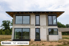 Nasze realizacje – Wiśniowski – Brama segmentowa UniTherm, okna PVC PRIMO 82, rolety zewnętrzne  Szukasz stolarki dla swojego domu, który ma być zarówno estetyczny, jak i energooszczędny? Zobacz naszą realizację, gdzie zastosowaliśmy kompleksowe rozwiązania Wiśniowski, gwarantujące funkcjonalność i niezawodność.  Lokalizacja realizacji: Drozdów  Okna PVC PRIMO 82 W tym projekcie postawiliśmy na okna PVC PRIMO 82, które wyróżniają się  świetnymi właściwościami izolacyjnymi. Na zewnątrz są w nowoczesnym kolorze - ciemnoszary jedwab, który idealnie pasuje do współczesnej architektury. Wewnątrz okna pozostały klasycznie białe (RAL 9016). Dodatkowo okna charakteryzuje bogate wyposażenie jak ciepłe ramki, zabezpieczenia antywłamaniowe, blokady antyprzeciągowe czy okucia z ukrytymi zawiasami.  Profil okien: PRIMO 82 Kolor zewnętrzny: Ciemnoszary jedwab Kolor wewnętrzny: Biały RAL 9016 Okucia: MACO MultiPower - zawiasy ukryte Wyposażenie: ciepła ramka, dwa zaczepy antywyważeniowe i najazd dolny, blokada antyprzeciągowa  Rolety Zewnętrzne Protecta P Dla zapewnienia prywatności i bezpieczeństwa zamontowaliśmy elektrycznie sterowane rolety zewnętrzne Protecta P. Ich pancerz PA-39 w kolorze szarego antracytu doskonale współgra z ramami okiennymi, tworząc spójną i elegancką całość. Rolety te to nie tylko świetna ochrona przed słońcem i hałasem, ale także dodatkowa bariera utrudniająca włamanie.  Rolety: Protecta P sterowane elektrycznie Pancerz: Pancerz PA-39 Kolor: Szary antracyt  Brama Segmentowa UniTherm Całość dopełnia nowoczesna brama segmentowa UniTherm w kolorze RAL 7016 (antracyt). Dzięki panelom typu G (bez przetłoczeń) brama wygląda minimalistycznie i bardzo elegancko, podkreślając nowoczesny styl budynku. Brama UniTherm to synonim najwyższej jakości, doskonałej izolacji termicznej i niezawodności, zapewniając łatwy i bezpieczny dostęp do garażu dzięki automatyce Wiśniowski SPARK 1100.  Brama: Segmentowa UniTherm Kolor: RAL 7016 Typ panela: G – bez przetłoczeń Automatyka: Wiśniowski SPARK 1100